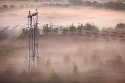 Electric tower and wires on field in fog