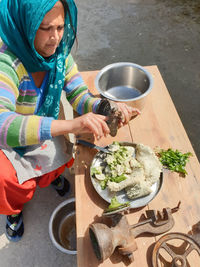 A indian woman taking out wet black gram from an old hand grinding mill machine at home