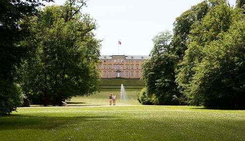 Man and woman walking on grassy field against frederiksberg palace