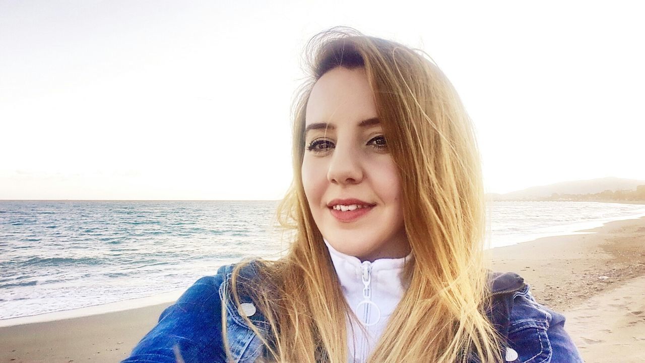 beach, young adult, sea, long hair, young women, portrait, person, looking at camera, lifestyles, leisure activity, clear sky, water, shore, front view, horizon over water, headshot, smiling