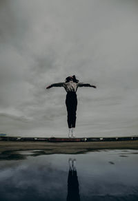Full length of woman jumping by water against sky