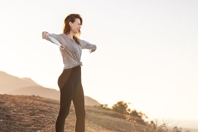 Woman standing with arms raised against sky during sunset