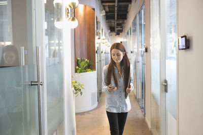 Young woman walking down office corridor checking her phone.