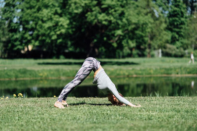 Full length of young woman exercising by pond on field