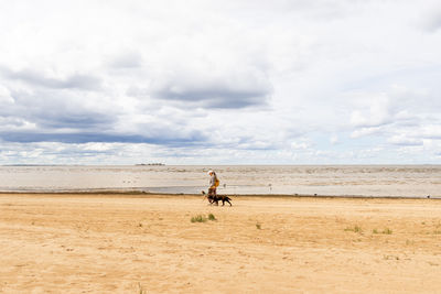 Rear view of woman walking at beach against sky