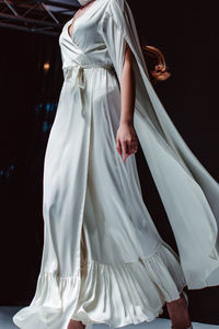 Elegant fashion details of white long silky bridal dress. fashion model walking on black background