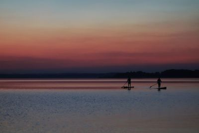 Silhouette people on sea against sky during sunset