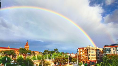 Rainbow over buildings against cloudy sky