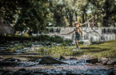 Boy holding stick by stream on field