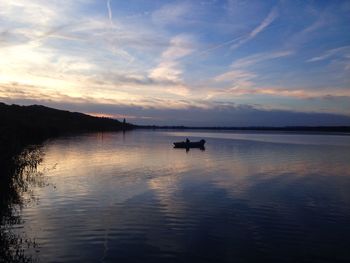 Silhouette boat moored at lake against sky at dusk