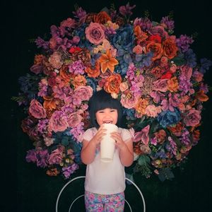 Portrait of cheerful girl with drink standing against large flower bouquet