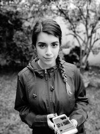 Portrait of smiling young woman holding mobile phone while standing on land