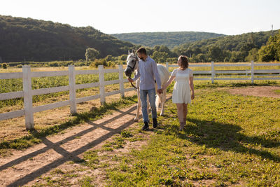 Rear view of two people standing on grassland against plants