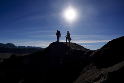 Silhouette man and woman walking on mountain against sky during sunset