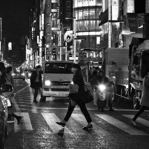 People walking on street amidst illuminated buildings in city at night