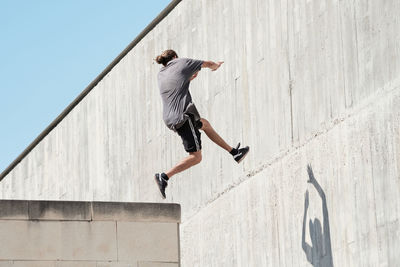 Side view of courageous young male jumping on concrete wall of building while performing dangerous stunt and doing parkour in city