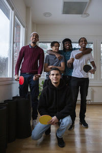 Boy crouching in front of smiling friends in games room