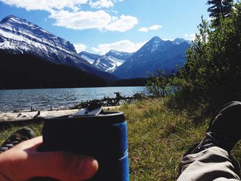 Low section of people relaxing in front of snowcapped mountains against sky