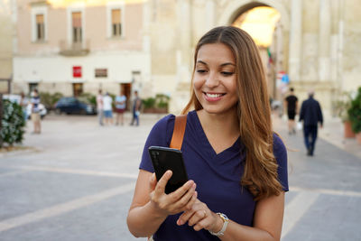 Close up portrait of a happy young woman walking in the city sending text message on cellphone