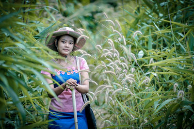Portrait of young woman wearing hat standing by plants on field