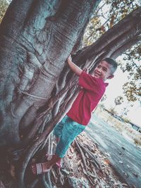 Smiling boy standing by tree trunk