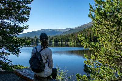 Rear view of woman sitting by lake against sky