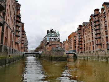 Canal amidst buildings in city against sky
