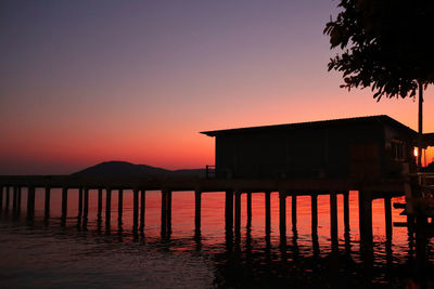 Silhouette house by lake against orange sky