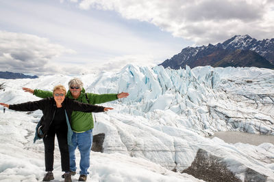 Portrait of senior man and woman with arms outstretched hiking on snowcapped mountains