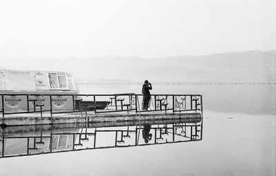 Man standing on railing by sea against clear sky