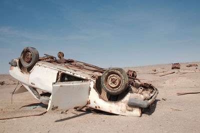 Old rusty car on sand against sky