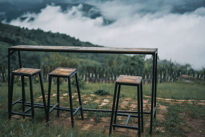 Empty chairs and table on field against sky