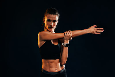 Portrait of young woman exercising against black background