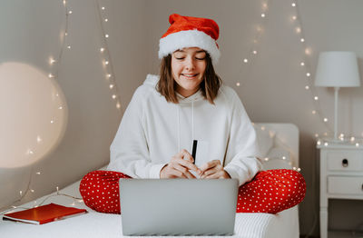 Girl wearing santa hat using laptop while sitting on bed