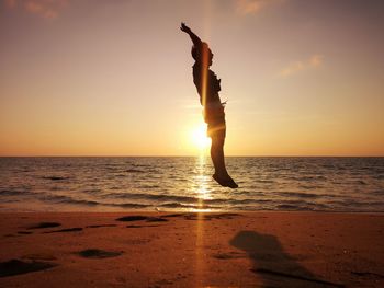 Silhouette man jumping at beach against sky during sunset