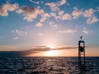 Silhouette tower by sea against sky during sunset