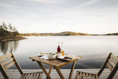 Food arranged on table by lake against sky
