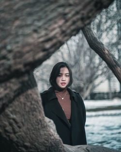 Portrait of young woman standing by tree during winter