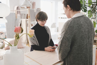 Female customer using smart phone in front of owner at upholstery store