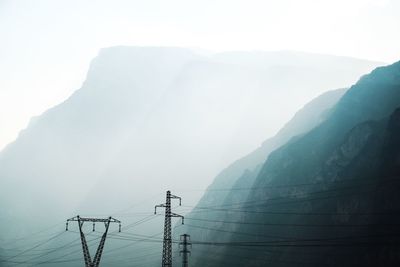 Electricity pylon on mountain against sky during foggy weather