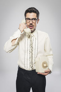 Man talking on rotary phone while standing against white background