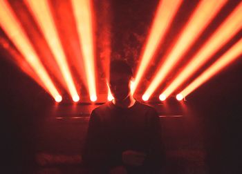 Silhouette man standing by illuminated lights at night