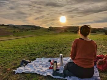 Man sitting on field against sky during sunset