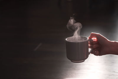 Silhouette of a female hand with a mug of hot drink - coffee or tea with steam on a black background