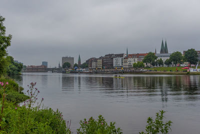 Buildings at waterfront against cloudy sky