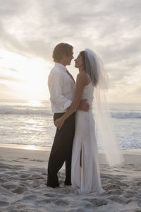 Rear view of couple kissing at beach against sky