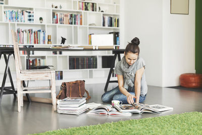 Female architect reading magazine on floor at home office