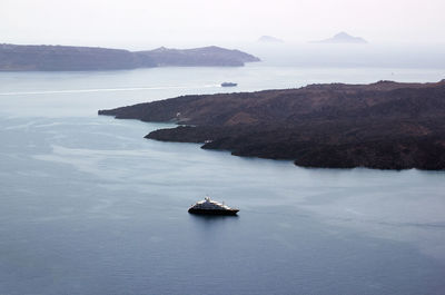 Wide angle aerial drone shot of a cruise ship sailing around volcanic island of santorini