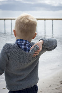 Rear view of boy throwing stone while standing at beach