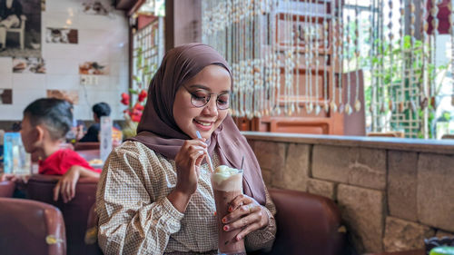 Portrait of smiling young woman using mobile phone while sitting at restaurant